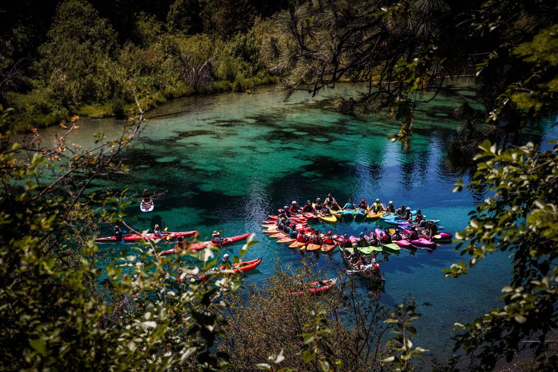 Members of Paddle Tribal Waters, an indigenous youth kayaking program, holding hands in a circle while in kayaks on a lake